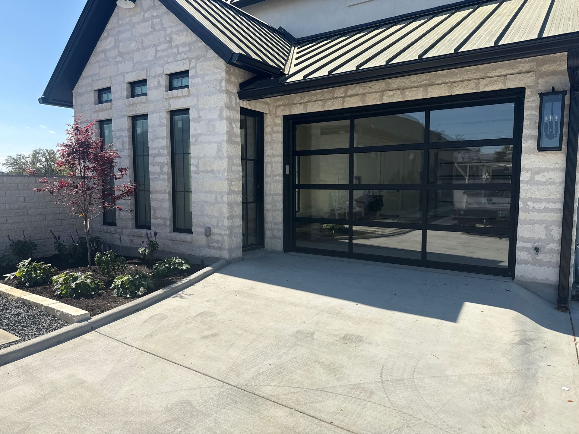 Modern stone house exterior with a black garage door and wide concrete driveway