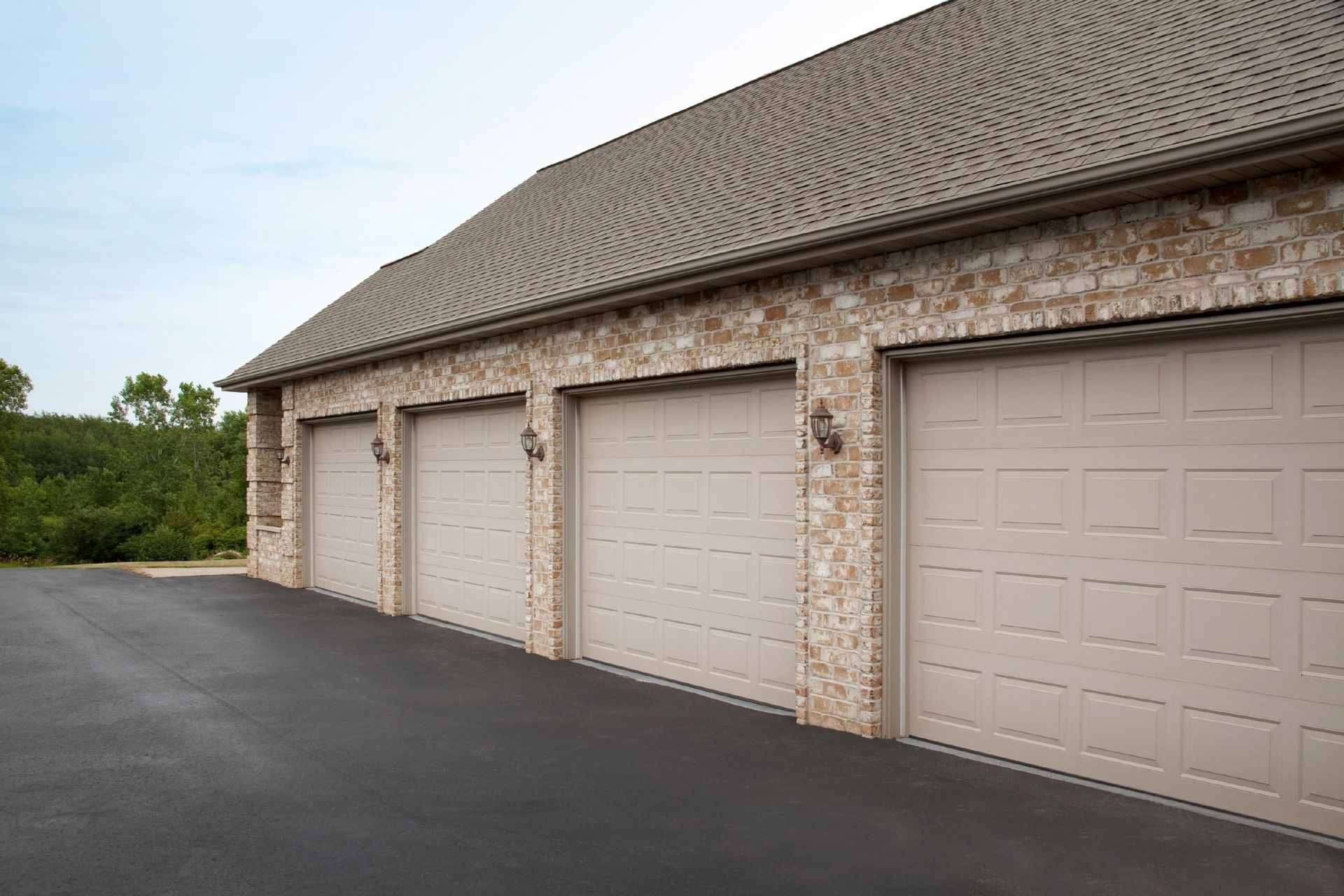 Row of beige garage doors on a brick building beside a paved driveway
