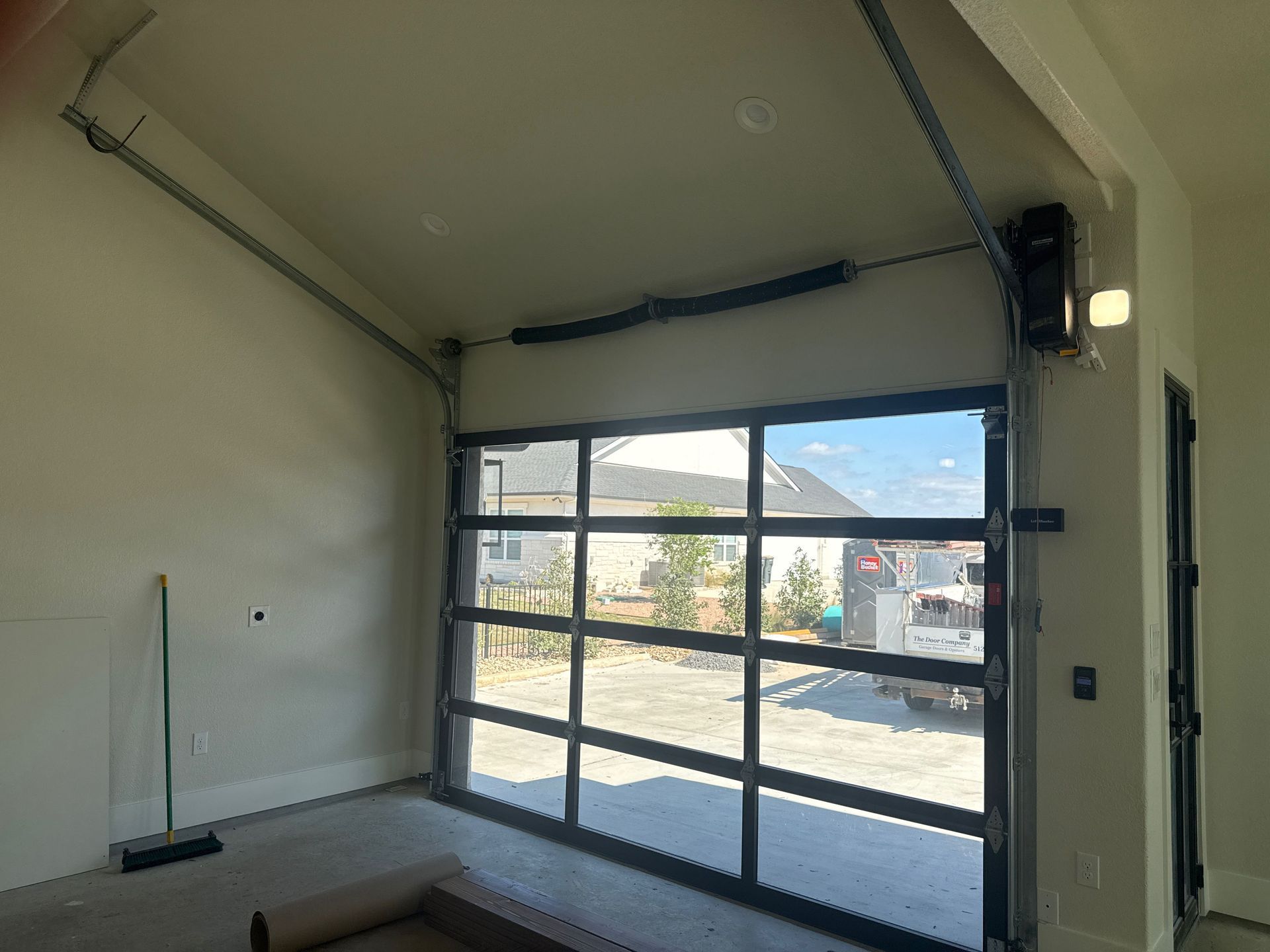 Empty garage with a partially open glass door, broom, and light-colored walls.