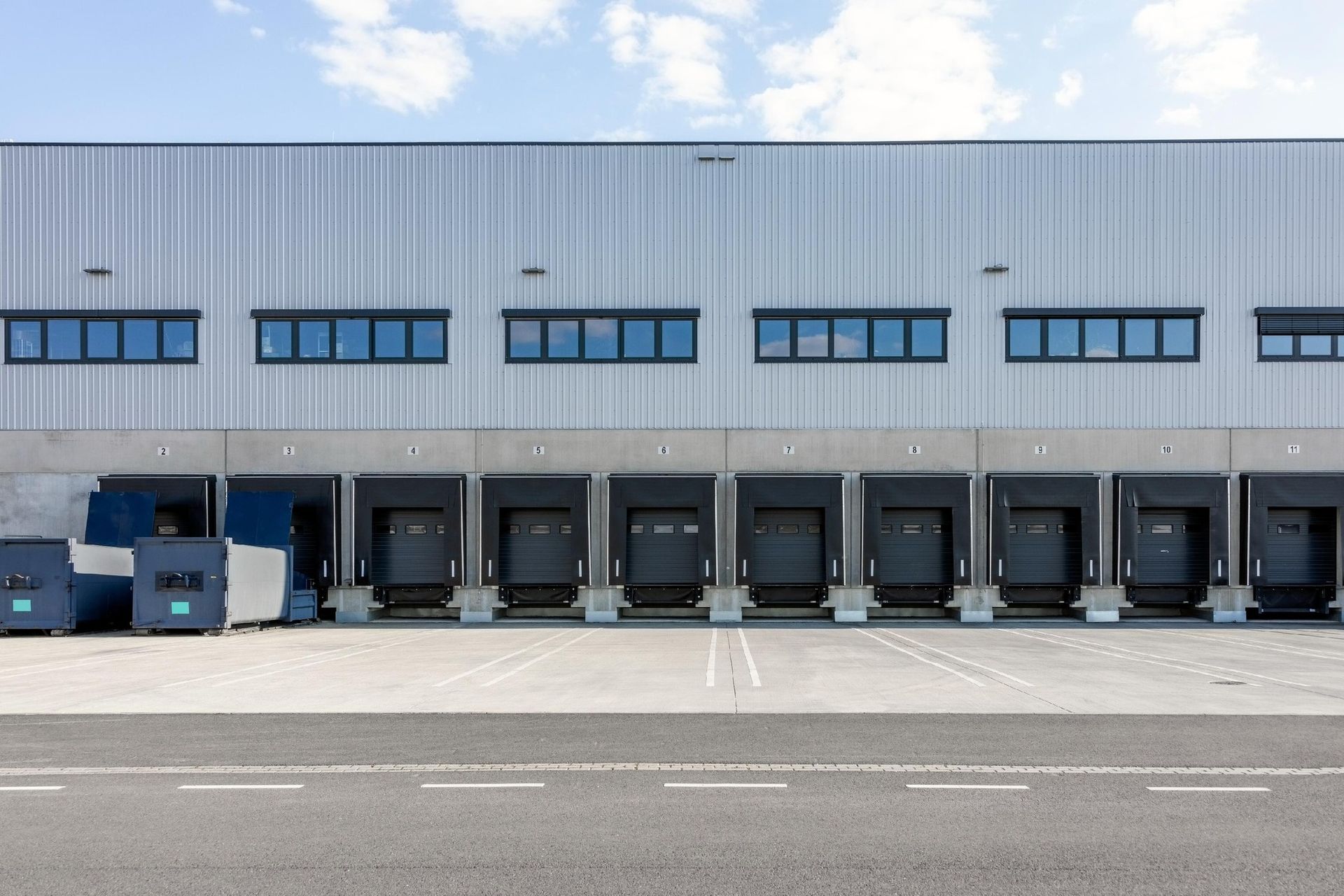 Row of warehouse loading docks with parked trucks and trailers outside a gray industrial building