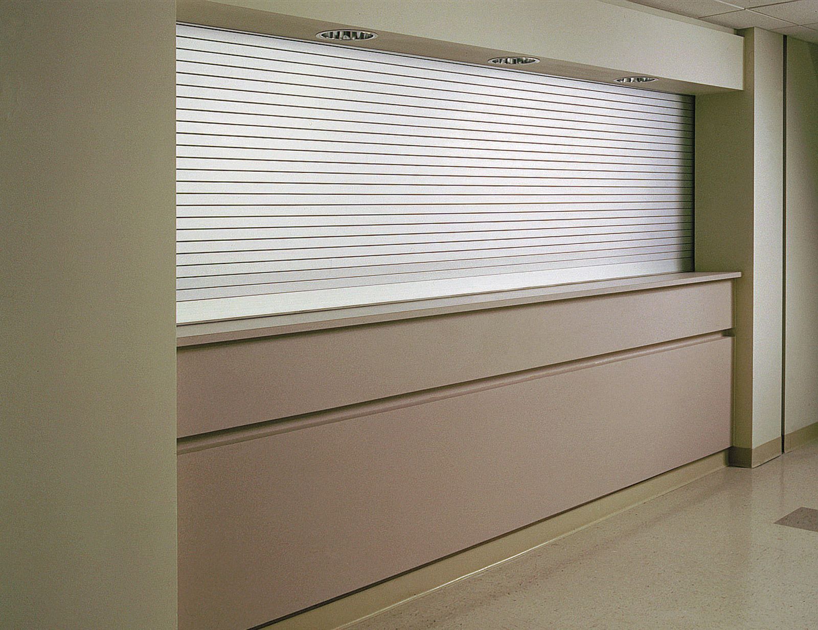 Closed service counter with beige panels and a white patterned window in a hallway