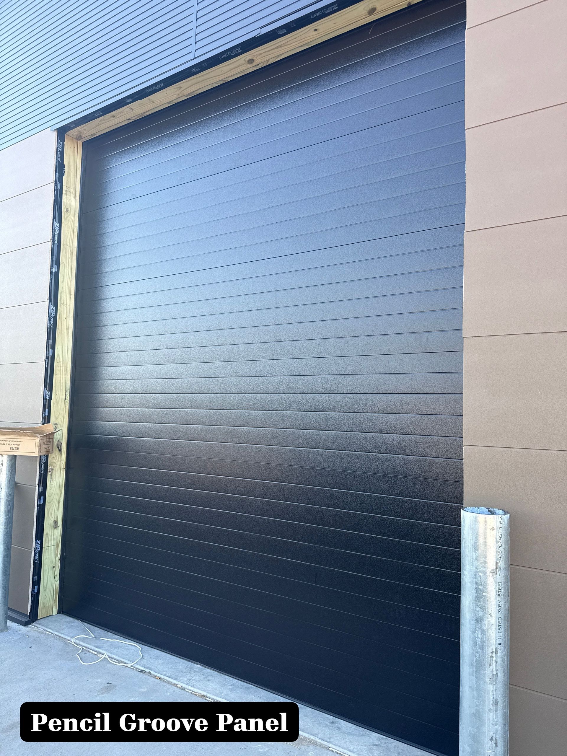 Black steel roll-up door with a grooved, dimpled surface in an industrial setting
