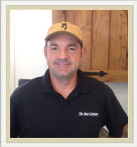 Man in yellow cap and black polo shirt standing indoors in front of a wooden door