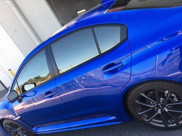 A blue car with black wheels is parked in front of a building.