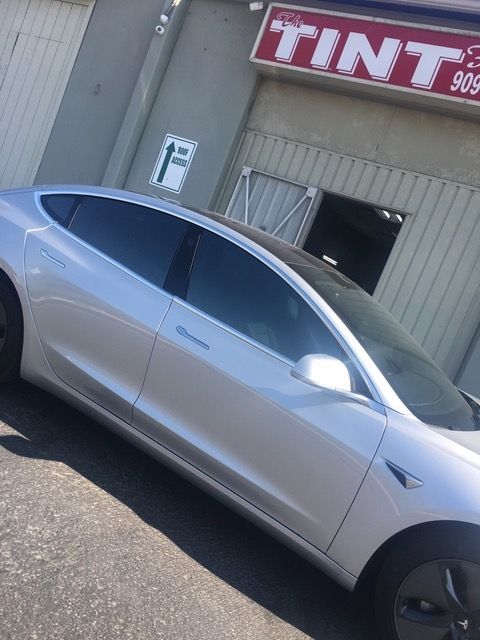 A silver car is parked in front of a tint shop.