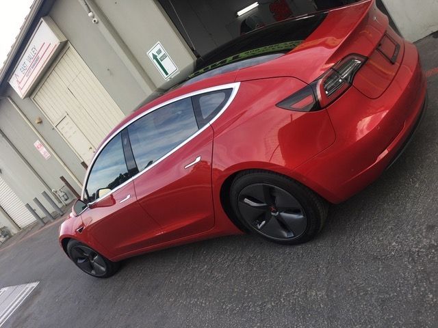 A red tesla model 3 is parked in front of a building.