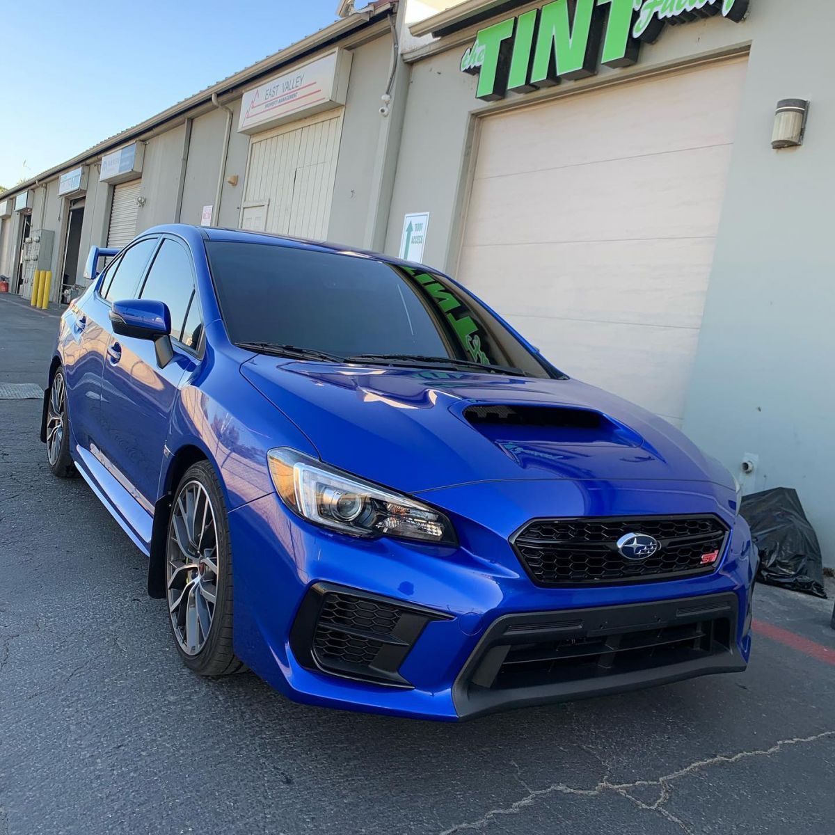 A blue car is parked in front of a building that says tint.