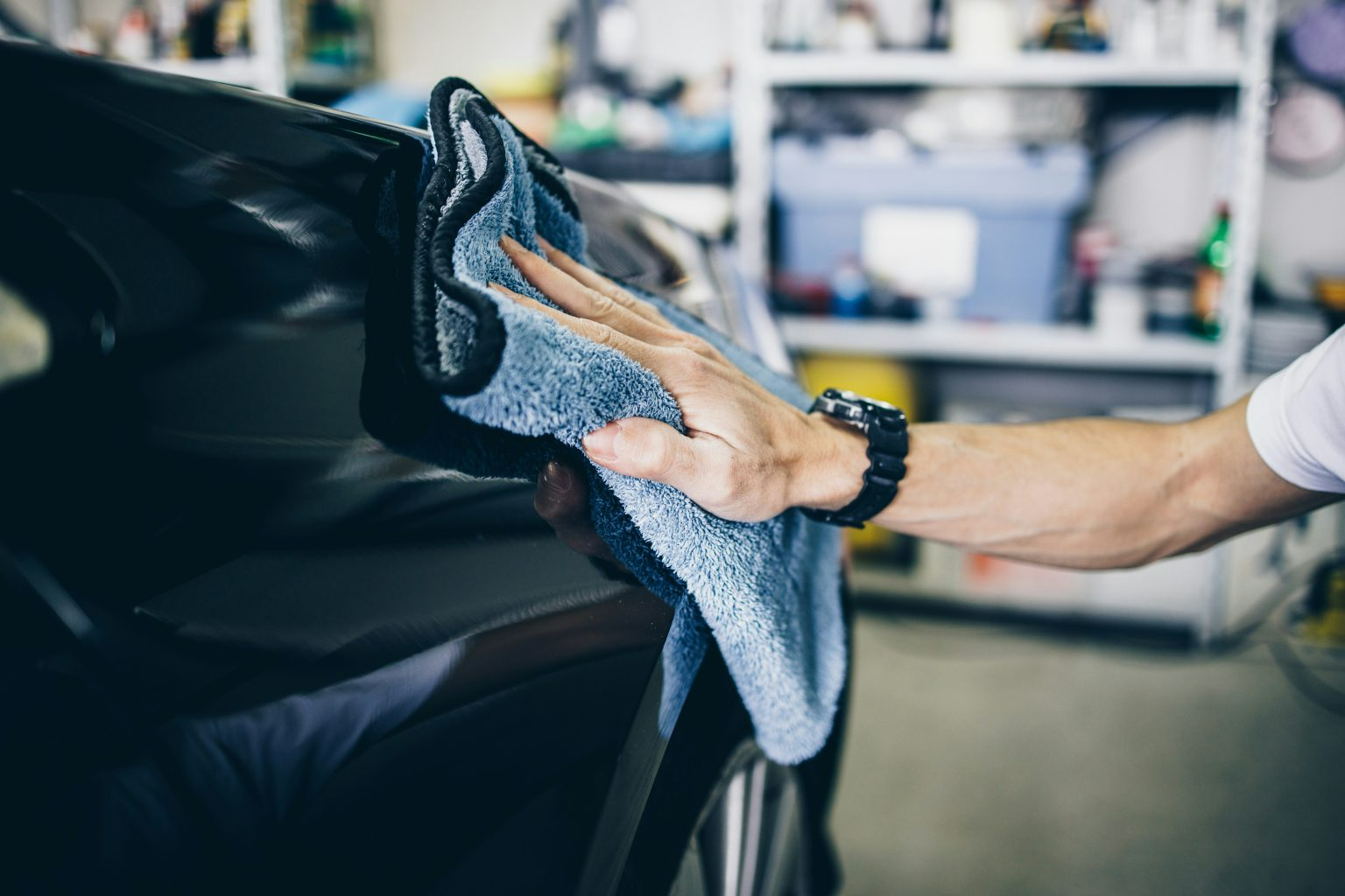 A man is cleaning a car with a towel in a garage.