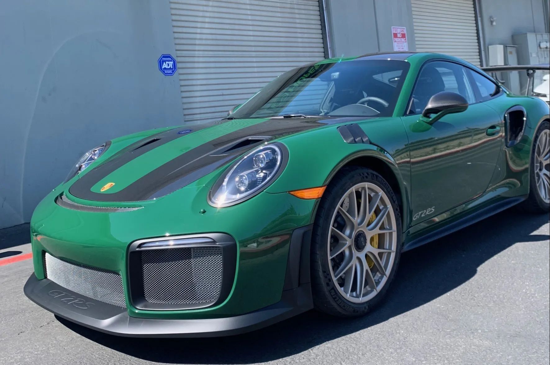 A green porsche 911 gt2 rs is parked in front of a building.