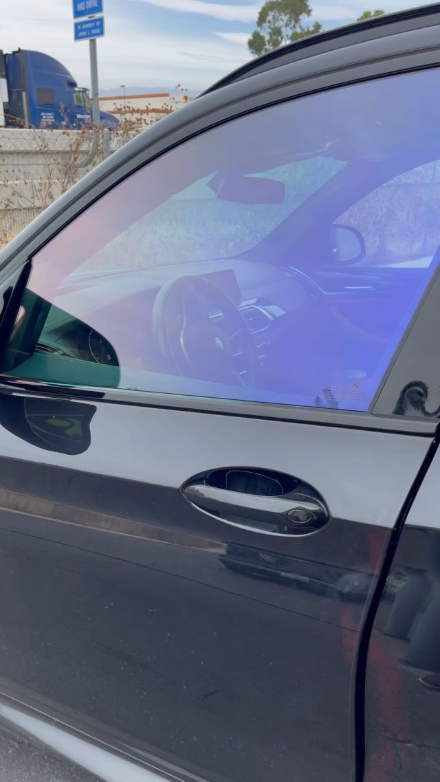 A black car with a purple window tint is parked in a parking lot.