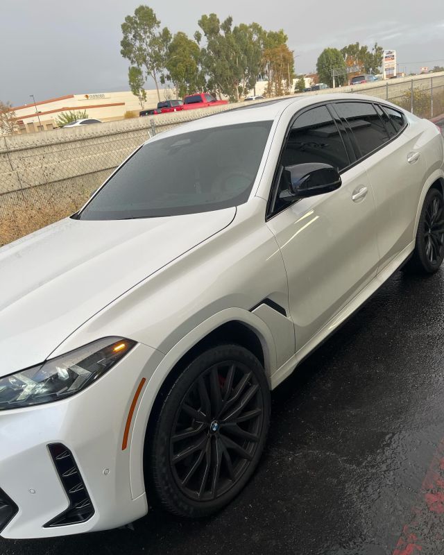 A white car is parked in a parking lot on a rainy day
