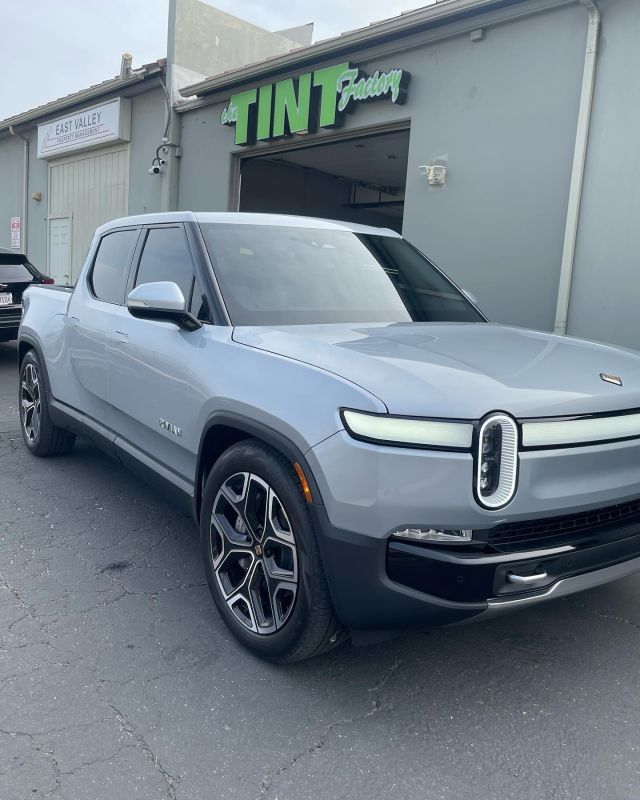 A gray car is parked in front of a building that says tint