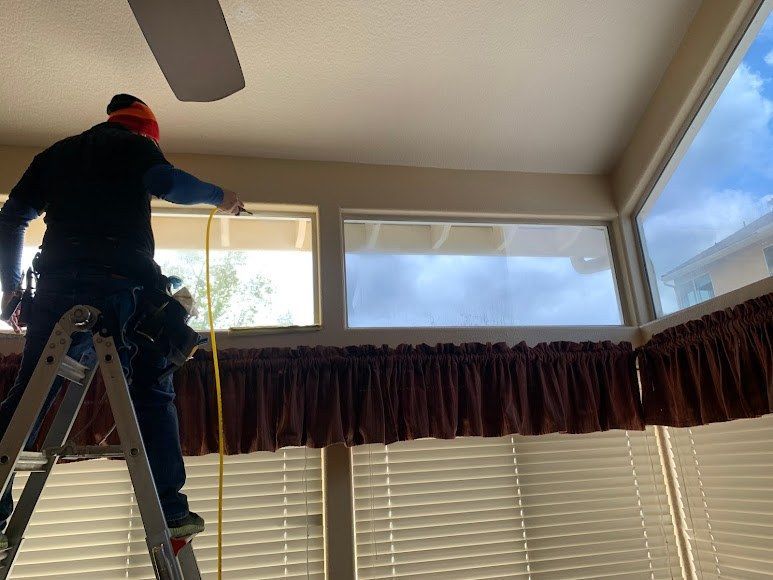 A man is standing on a ladder measuring a window.