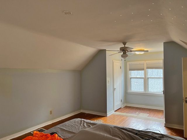 Bedroom with sloped ceiling, light blue walls, wood floor, ceiling fan, and a window.