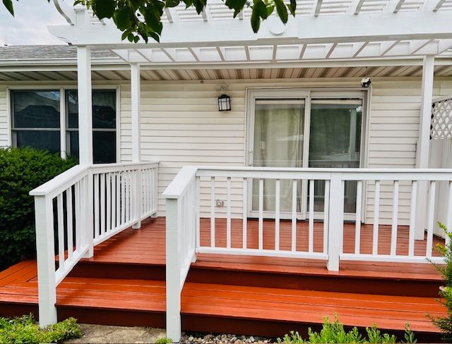 White deck with red-painted floor, white railing, and pergola, in front of a house.