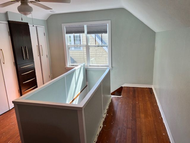 Bedroom with hardwood floors, white railing, window, and built-in dark cabinets. Walls are light green.