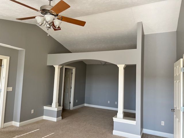 Gray-painted room with white architectural details, featuring columns, an arched opening, a ceiling fan, and a door.
