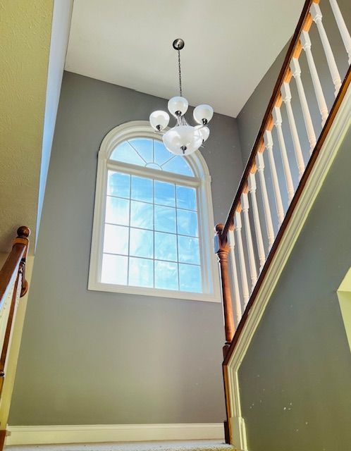 Staircase with gray walls, large window, and chandelier. Sunlight streams in.