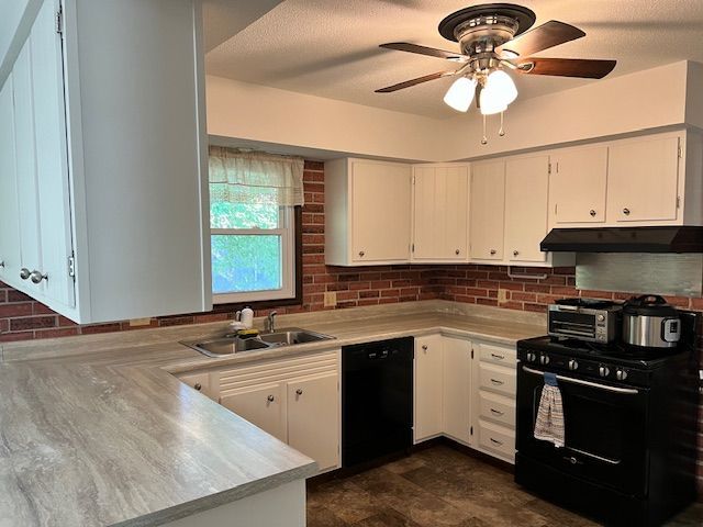 White kitchen cabinets and counters, brick backsplash, black appliances, window.