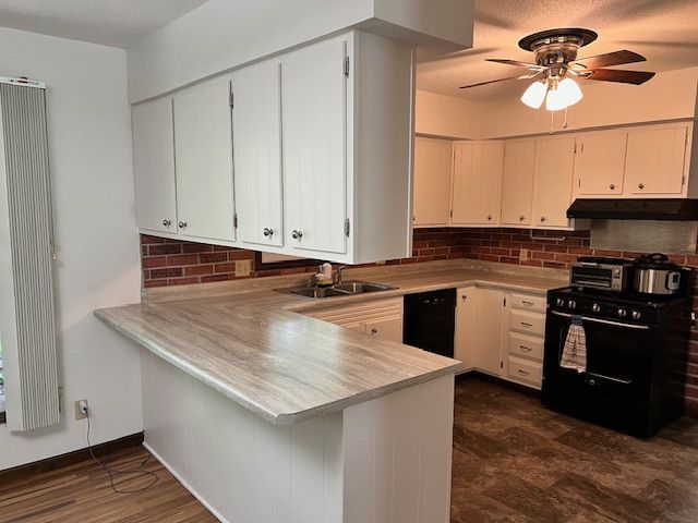 Kitchen with white cabinets, beige countertops, black appliances, and brick backsplash.