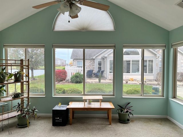 Sunroom with light green walls, windows overlooking a backyard, and a brown ceiling fan.