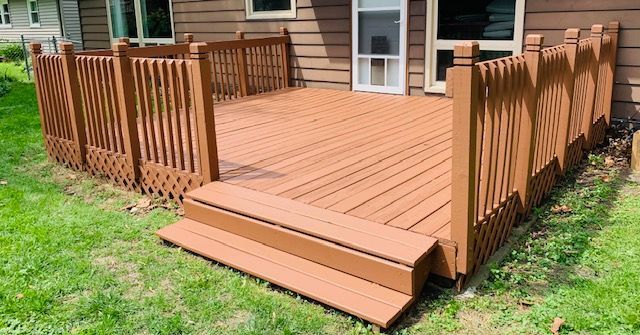 Brown wooden deck with steps, railings, and latticework, in a grassy backyard.