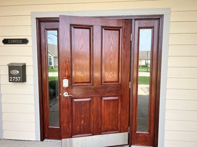 Wooden clubhouse entry doors, one ajar. Address plate, mailbox. Light-colored siding.