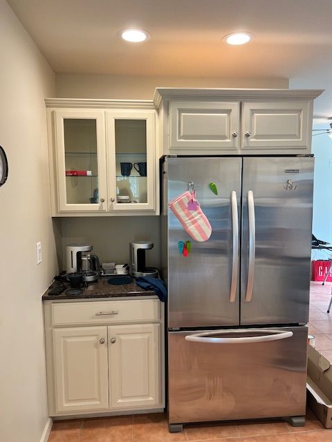 Kitchen with stainless steel refrigerator and light gray cabinetry, including glass-front upper cabinets.
