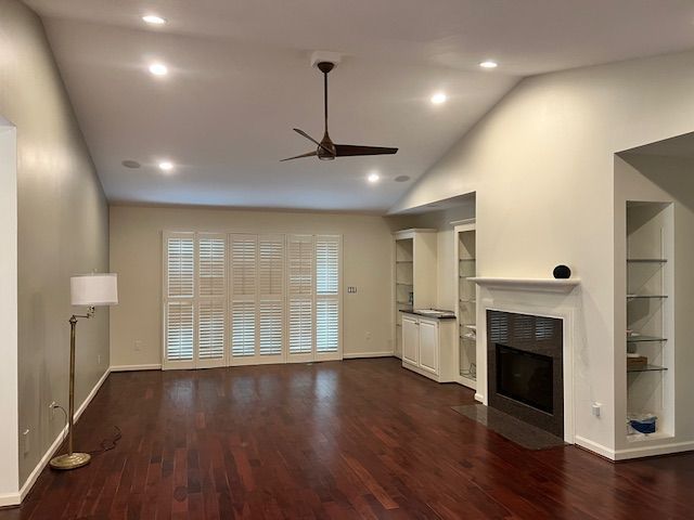 Living room with hardwood floors, white walls, built-in shelves, fireplace, and window shutters.
