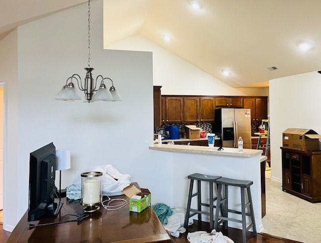 A light-filled kitchen and dining area with a chandelier, dark cabinets, and a desk.