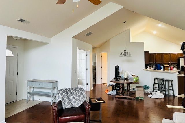 Living room with vaulted ceiling, hardwood floors, and a view into the kitchen. White walls and wooden cabinets.