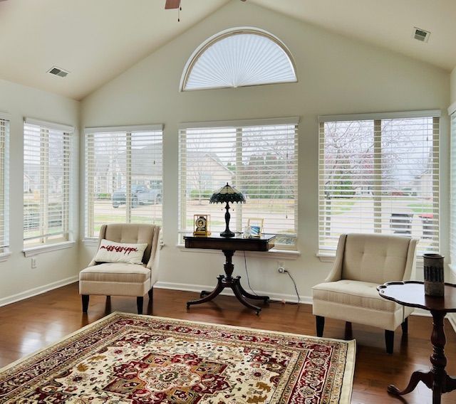 Sunroom with neutral walls, wood floor, arched window, two chairs, rug, and a table.
