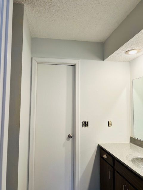 White bathroom with a closed door, dark vanity, and recessed lighting.