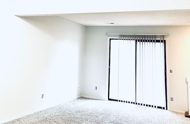 Empty white room with sliding glass door and vertical blinds.