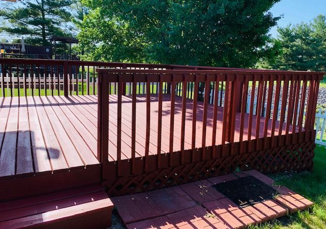 Red wooden deck with railing in a sunny yard.