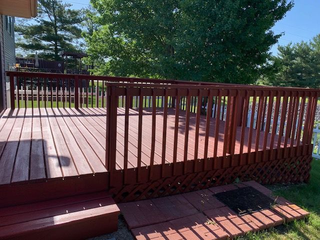 Red wooden deck with railing and steps outdoors on a sunny day.