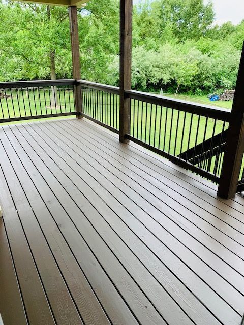 Wooden deck with brown planks and black railings overlooking a green yard and trees.