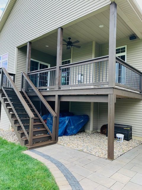 A two-story deck with stairs, a ceiling fan, and pebble ground covering.