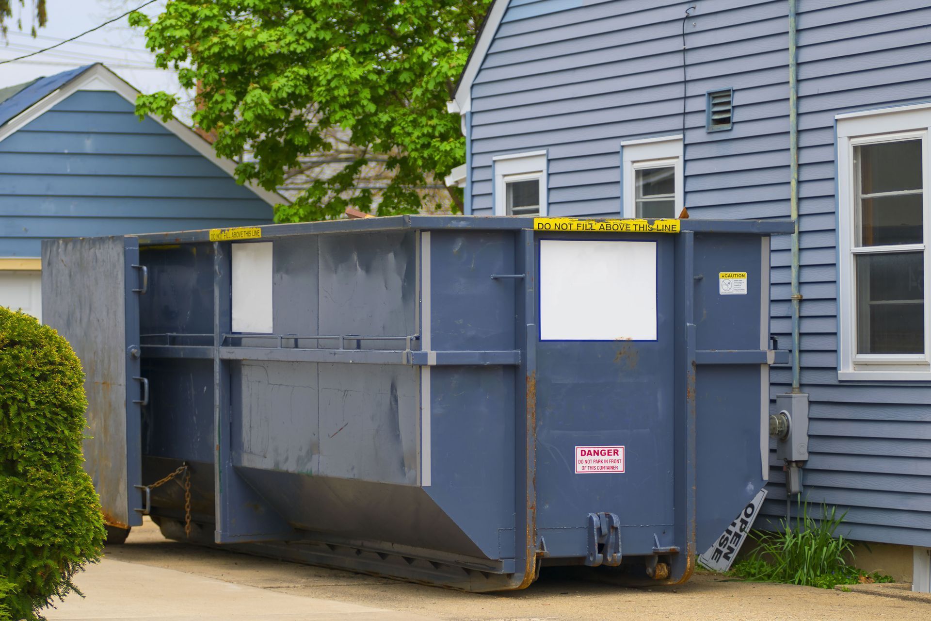 Blue dumpster parked next to a blue house, ready for waste disposal.