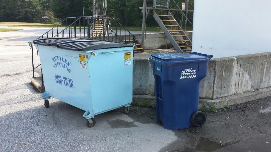 Blue dumpster and trash can next to a white building.