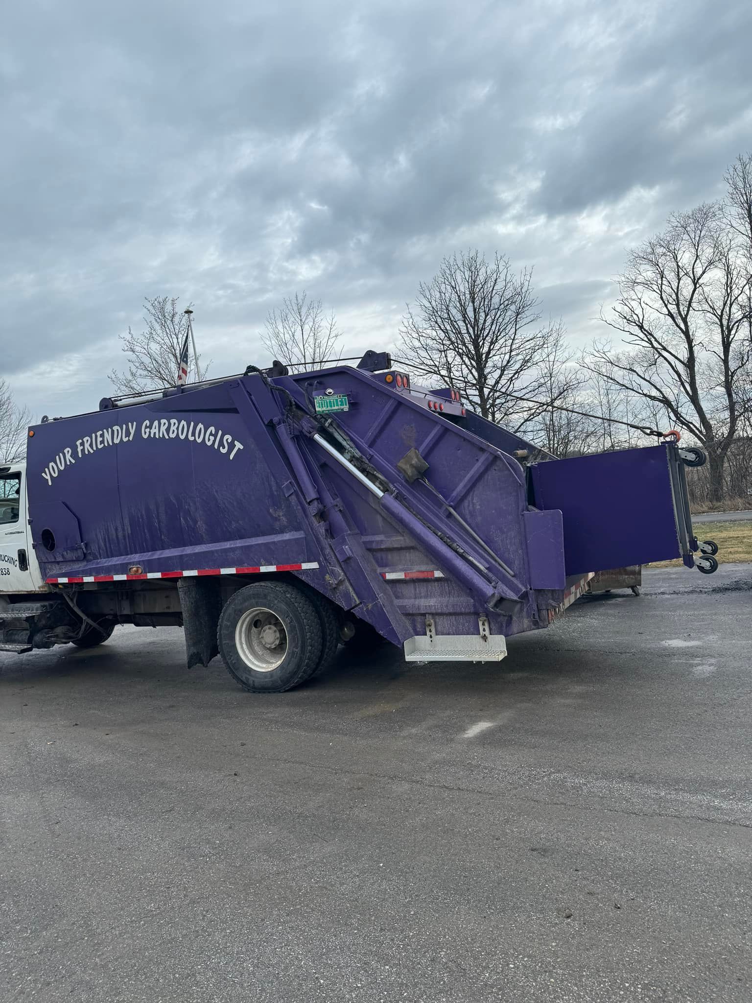 Purple garbage truck parked on asphalt. Overcast sky.