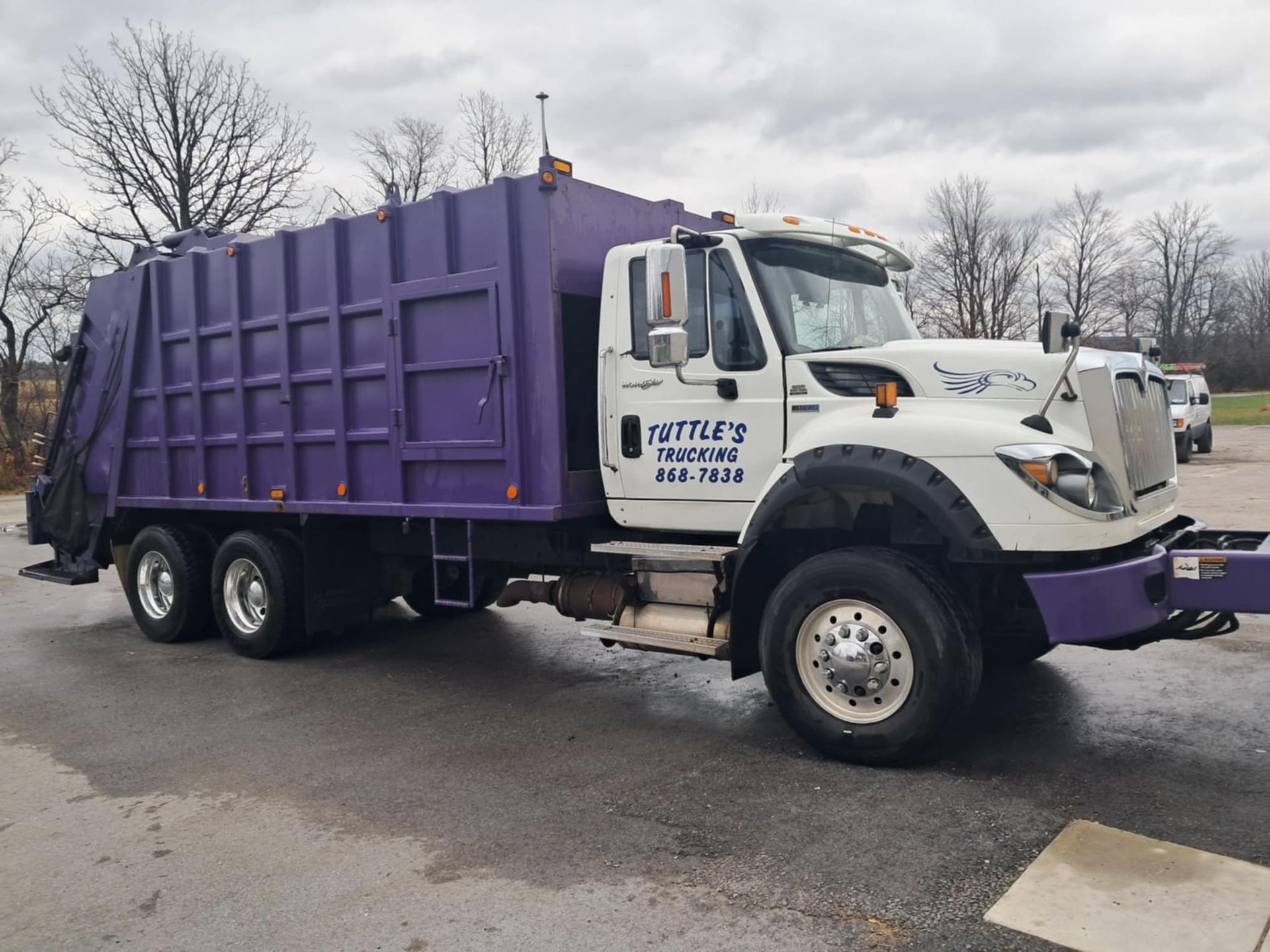 Purple and white garbage truck parked on asphalt.