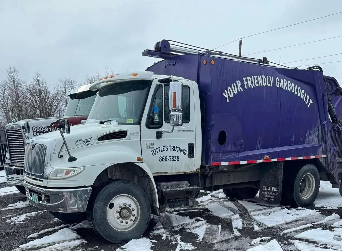White and purple garbage truck parked in snow, with text 