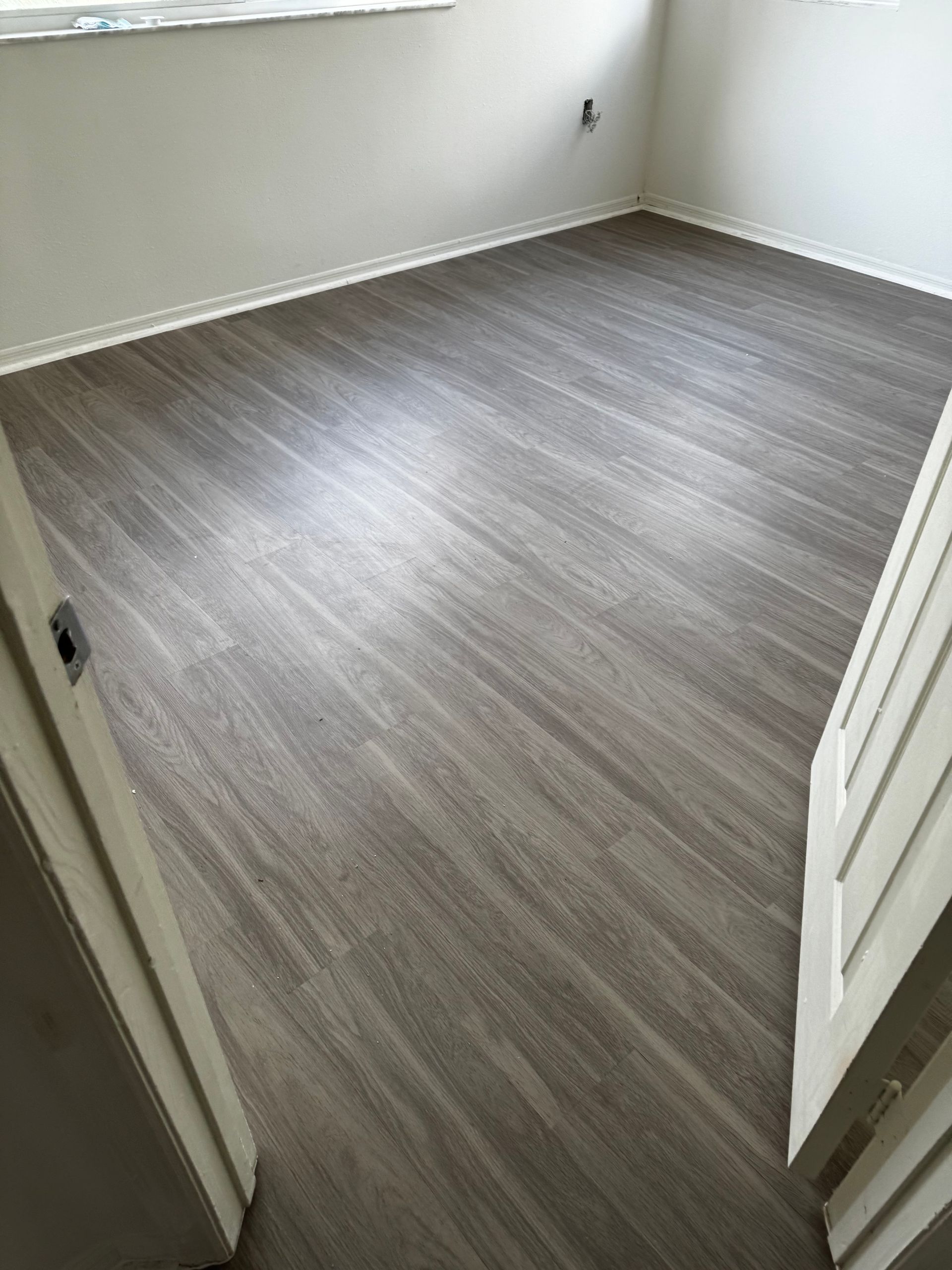 A bedroom with a vinyl floor and white walls.