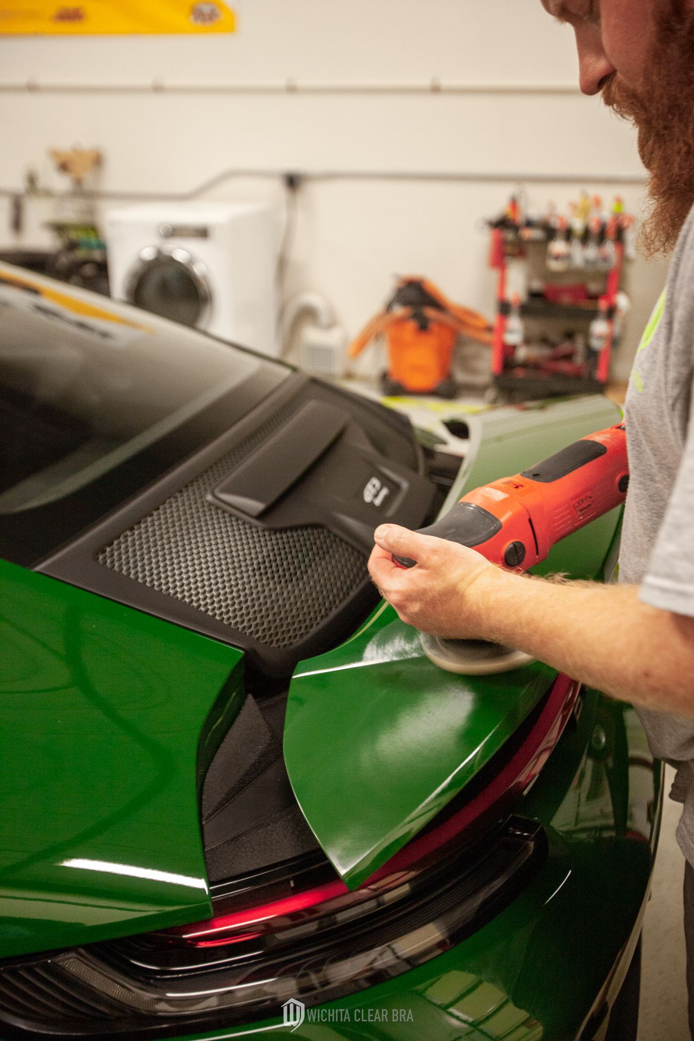 Detailer performing a one-step paint polish on the rear wing of a British Racing Green 2024 Porsche 911 GT3 Touring.
