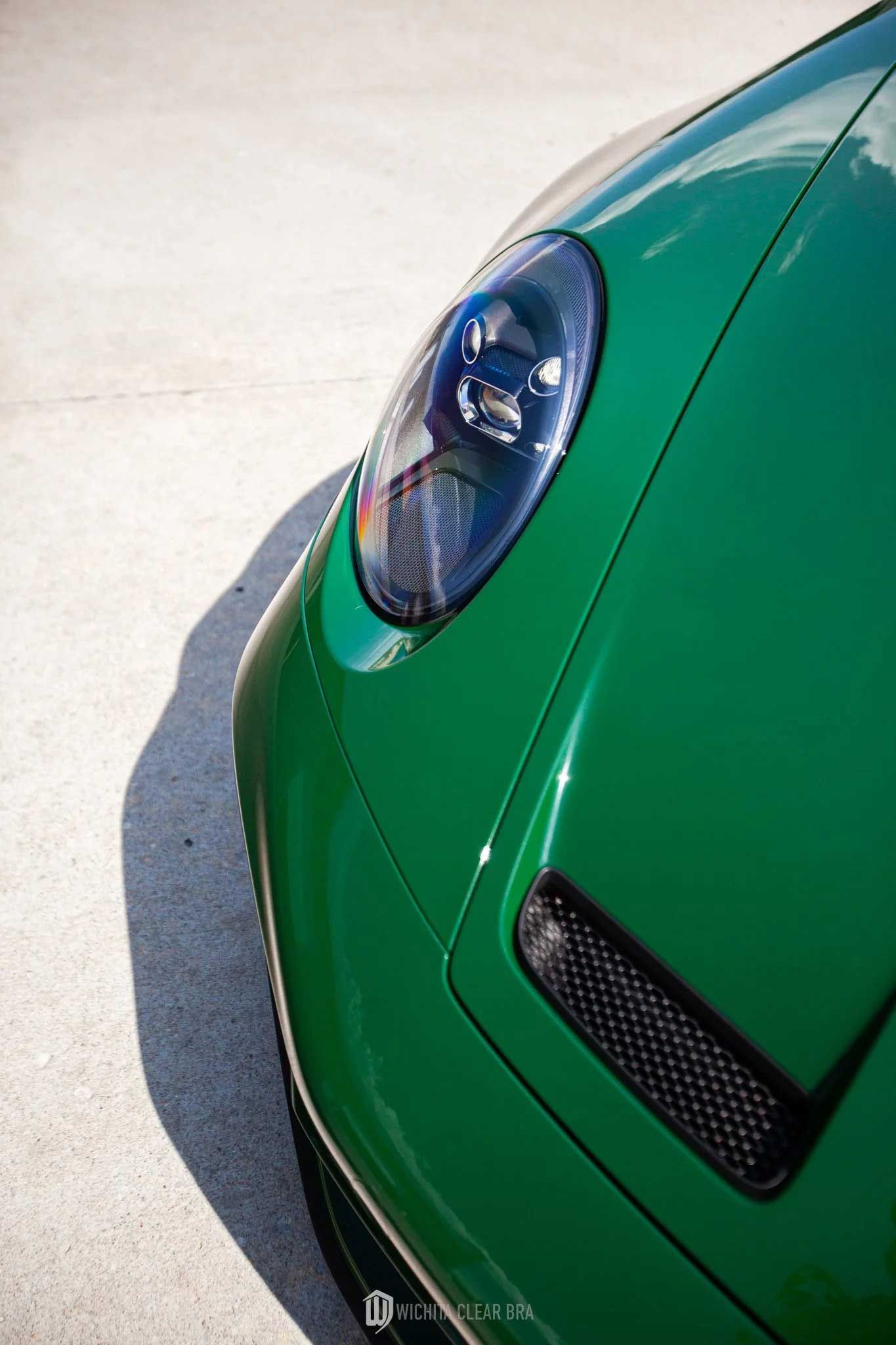 Green Porsche sports car's front with a headlight, air intake, and curved body.