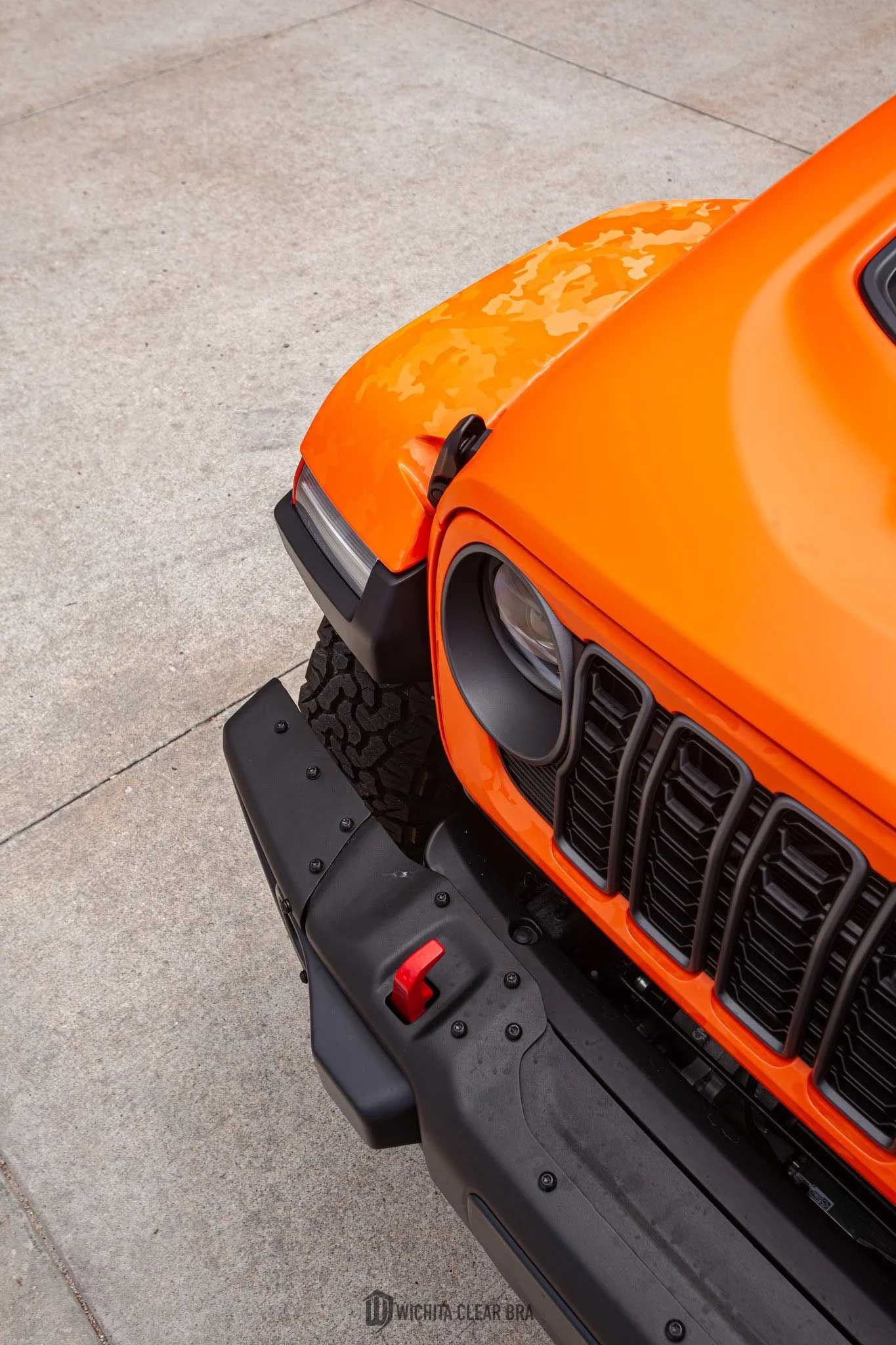 Orange Jeep front end with black grill and bumper on concrete.