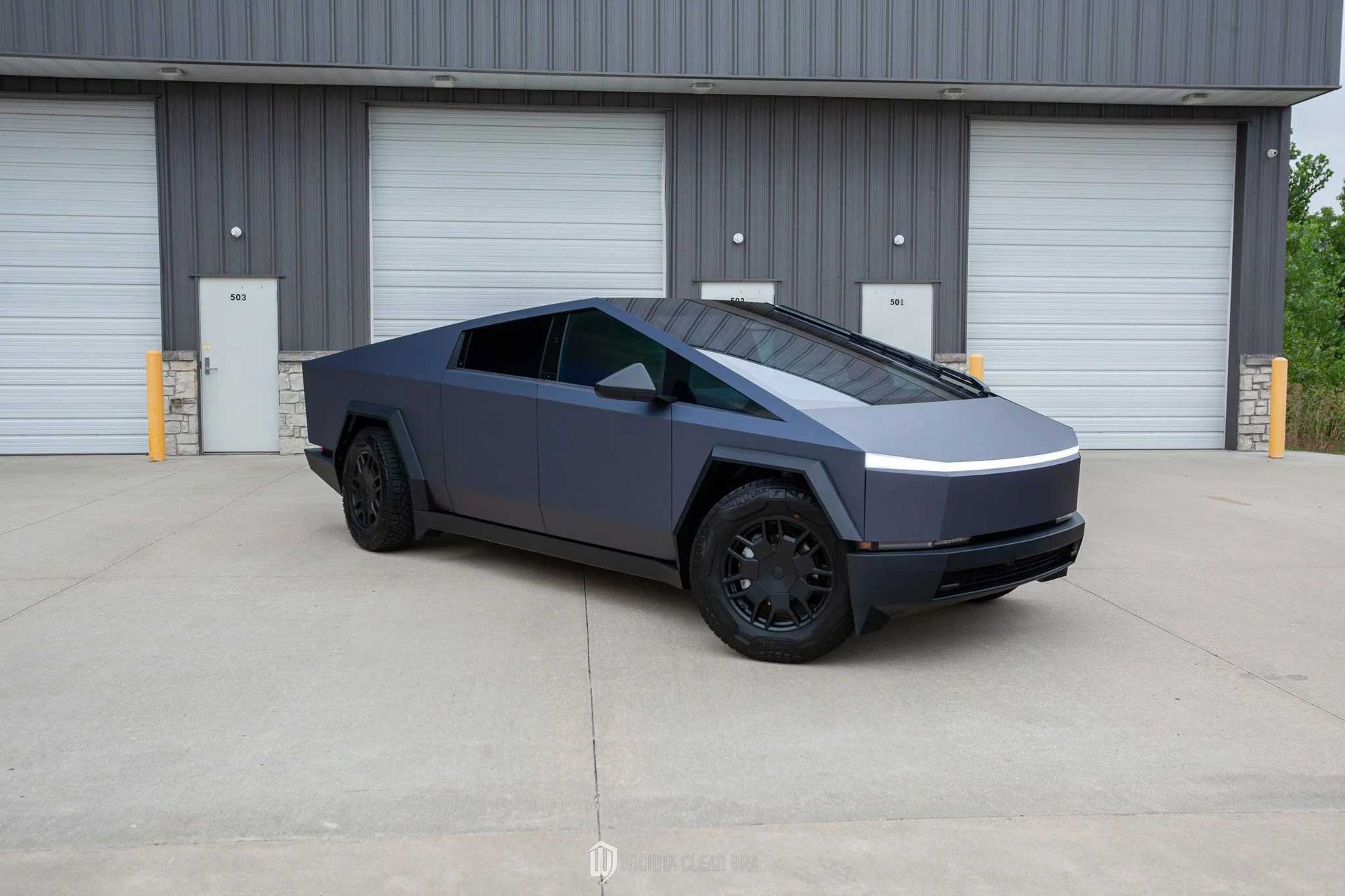 Gray Tesla Cybertruck parked in front of closed gray garage doors.