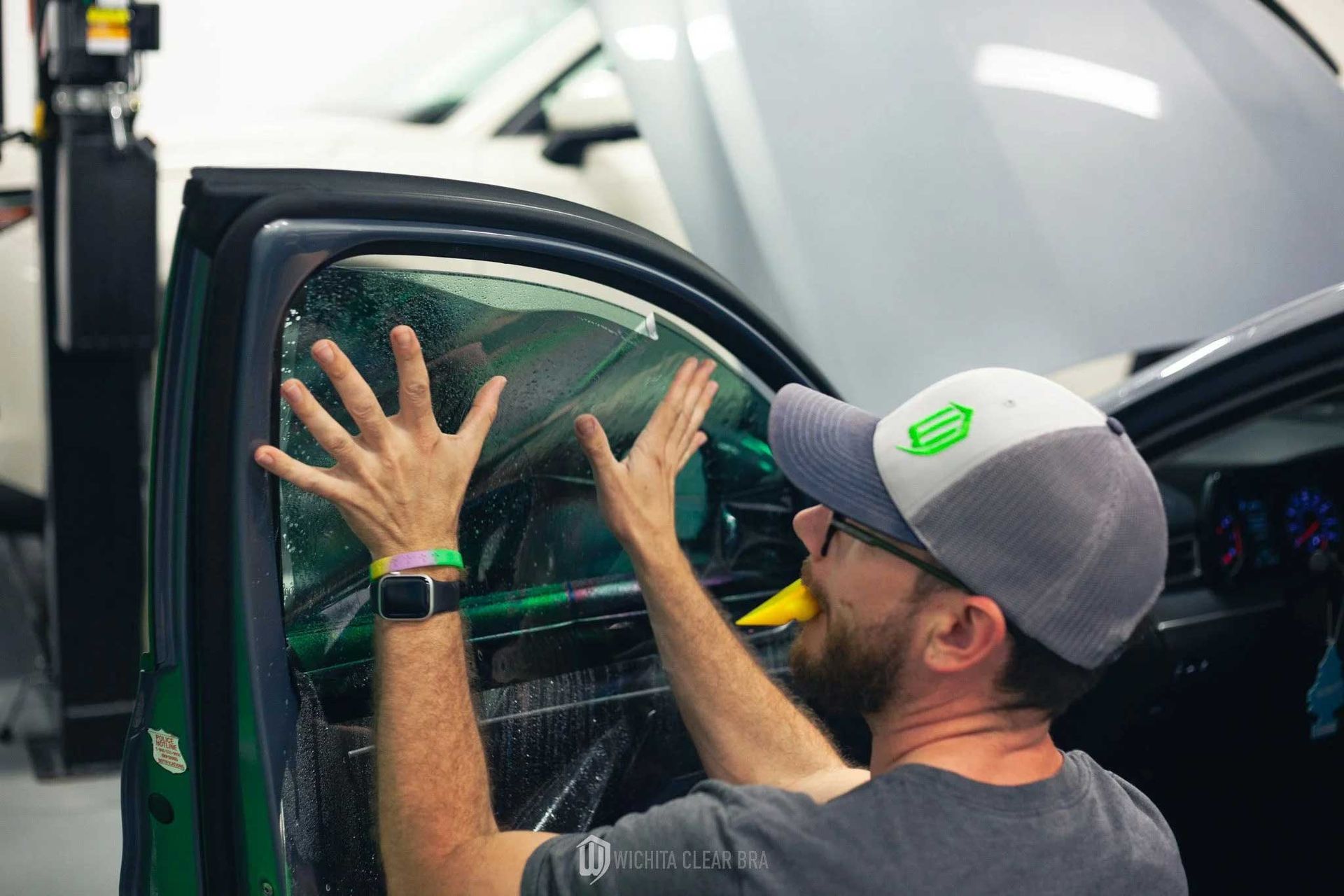 Person applying tint film to a car window in a garage.