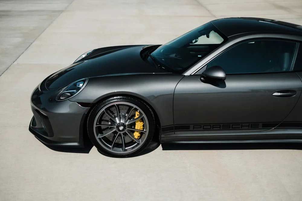 Dark gray Porsche sports car, with yellow brake calipers, parked on concrete.